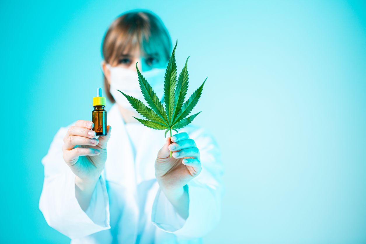 Glass template jar with CBD cannabis product and hemp leaf in hands of female doctor in neon light